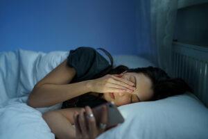 exhausted-woman-lying-in-bed-sleepless-hold-smartphone